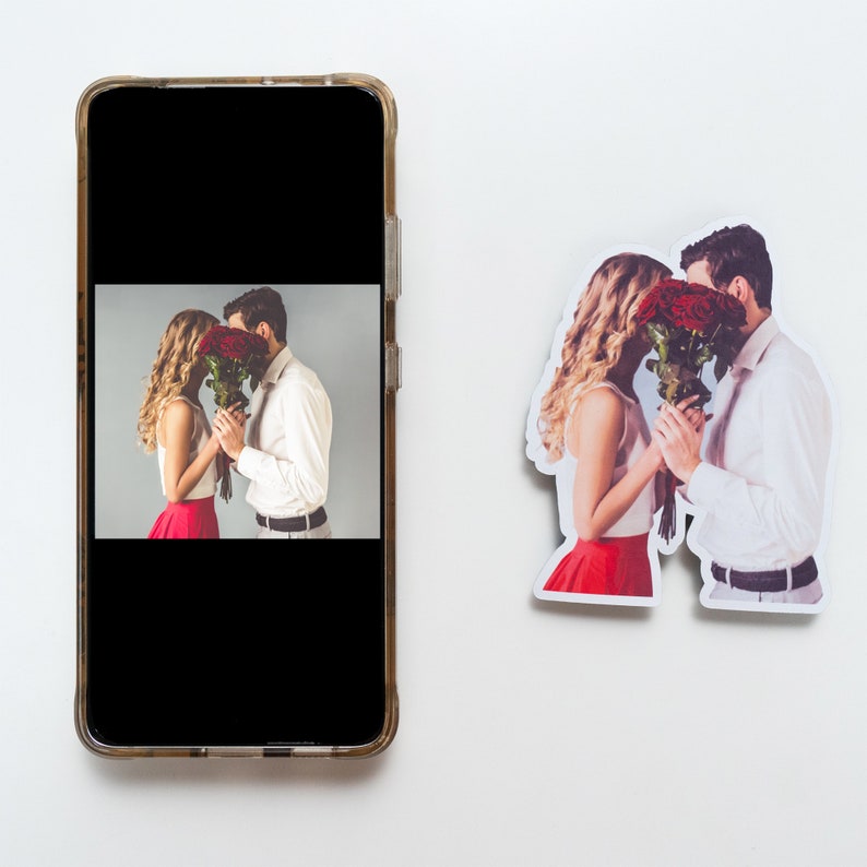 May include: A sticker of a couple kissing with a bouquet of red roses in front of their faces. The sticker is on a white background.