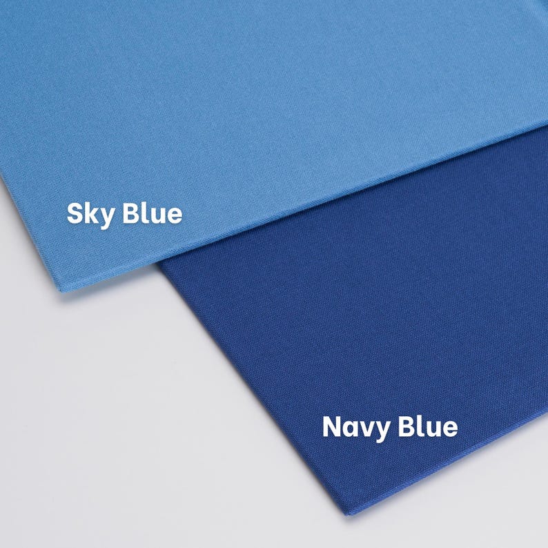 May include: Two rectangular fabric swatches featuring a smooth, solid-colored texture. The top swatch is light sky blue with the white text "Sky Blue" printed on it, while the bottom swatch is a darker navy blue with the white text "Navy Blue" printed.