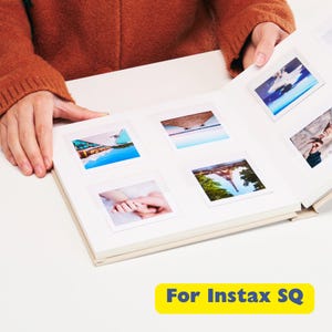 May include: A beige photo album open to display several Instax SQ photos. The photos are of various scenes, including landscapes and close-ups. The text "For Instax SQ" is in a yellow rectangle at the bottom.