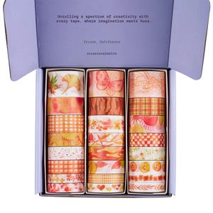 May include: A box containing 18 washi tapes. The tapes feature a variety of autumnal designs, including leaves, butterflies, and gingham patterns. The tapes are in shades of orange, yellow, and red.