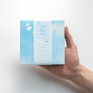 May include: A blue box with a white label that says "Ocean View" and features a design of clouds and seagulls. The label also says "Journal Stickers Gift Box" and "50 sheets".