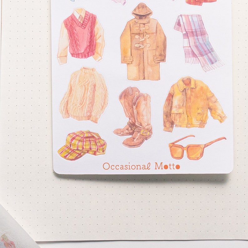 May include: A sheet of stickers featuring various clothing items, including a red sweater vest, a brown coat, a yellow jacket, a plaid scarf, a pair of brown cowboy boots, a plaid hat, and a pair of brown sunglasses. The text "Occasional Motto" is printed at the bottom of the sheet.