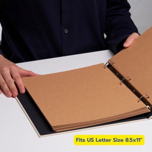 May include: An open scrapbook with brown pages and a white cover. The pages are held together by metal rings. The text "Fits US Letter Size 8.5x11" is visible in a yellow box.