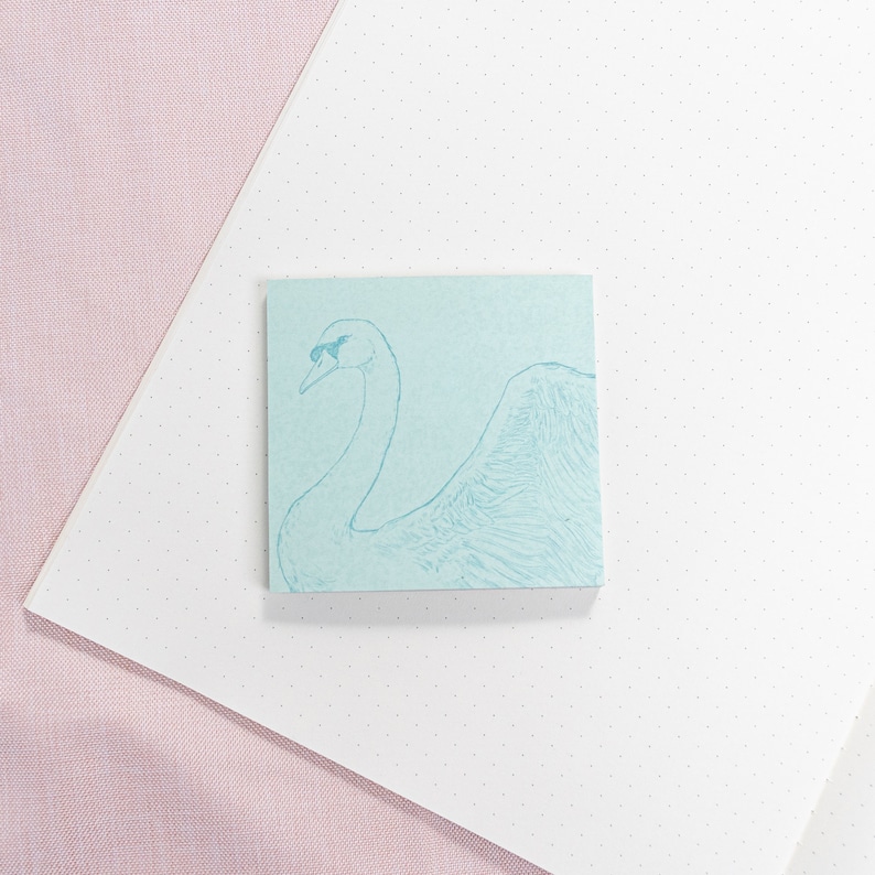 May include: A light blue sticky note with a line drawing of a swan on it. The swan is facing to the right and has its head tilted back.
