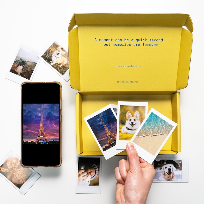 May include: A yellow box with a quote inside: "A moment can be a quick second, but memories are forever." The quote is attributed to "occasionalmotto" and "Irvine, California". The box is open and contains several instant photos of a dog, a beach scene, and the Eiffel Tower.