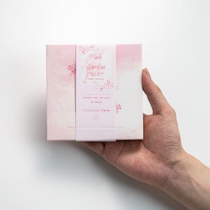 May include: A pink box with a floral design and the text "Pink Garden Journal Stickers Gift Box  Wasabi Stickers" and "Occasional Matte" on the front. The box contains 50 sheets of stickers that are 4x6 inches.