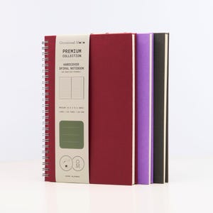 May include: Three hardcover spiral notebooks with a burgundy, purple, and black cover. The notebooks are part of the "Occasional Motto Premium Collection" and are labeled "Hard Cover Spiral Notebook".