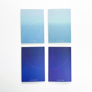 May include: Four small, blue and light blue notebooks with a gradient color design. Each notebook has the text "Occasional Marie" printed on the front.