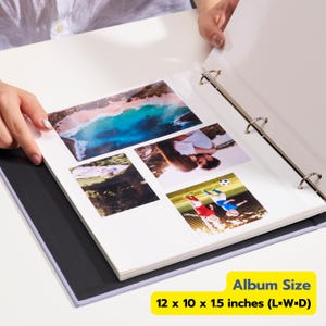 May include: A white three-ring binder photo album with a black interior lining, containing four color photographs on a white page. The album measures 12 x 10 x 1.5 inches. The photos depict a beach, a couple, a forest, and children playing soccer.