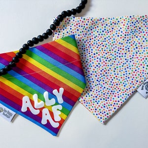 Puede incluir: Dos bandanas para perros, una con un patrón de rayas arcoíris y el texto "ALLY AF" en blanco, y la otra con un fondo blanco y un patrón de confeti de puntos de colores. Ambas bandanas tienen una pequeña etiqueta cosida con el texto "Sew Doggy Boutique".