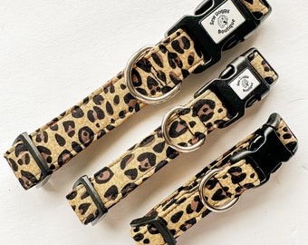 May include: Three leopard print dog collars with black buckles. The largest collar has the text "Sew Doggy Boutique" on the buckle.