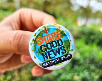 Puede incluir: Un botón redondo con el texto "I SHARE GOOD NEWS" en naranja y azul, con la referencia "MATEO 24:14". El botón tiene un diseño de mapa del mundo con tierra verde y océanos azules, rodeado por un borde blanco.