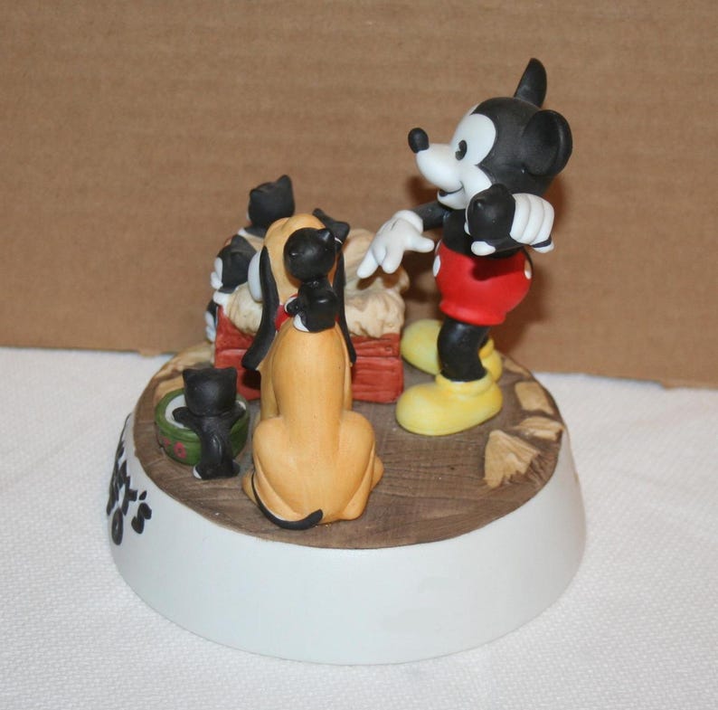 May include: A ceramic figurine of Mickey Mouse with Pluto and three kittens. Mickey is wearing red shorts and yellow shoes. Pluto is a brown and tan dog. The kittens are black and white. The figurine is on a white base with the words "It's a Dog's Life" written on it.
