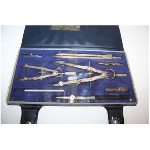 May include: A vintage drafting set in a blue case. The set includes several silver-colored compasses, dividers, and other drawing tools, neatly arranged on a blue velvet-like interior. The case is open, revealing the tools ready for use.