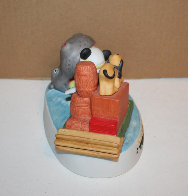 Puede incluir: Una figurita de cer&aacute;mica de Mickey Mouse, Donald Duck y Goofy en un barco con barriles y cajas. La figurita est&aacute; pintada en colores brillantes y tiene un estilo caprichoso.