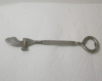 May include: A silver can opener with a hammer on one end and a bottle opener on the other. The handle is engraved with the text "ROYAL BANNER CIGARS 5c".