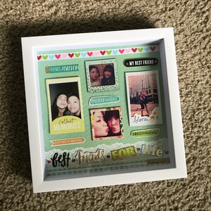 May include: A white picture frame with a green background and multiple photos of two friends. The photos are arranged in a collage style with decorative paper and stickers. The text "FRIENDS FOREVER", "MY BEST FRIEND", "PARTNER IN CRIME", "Collect MEMORIES", "FAVORITE PHOTOS", "bloom", "#BESTFRIEND", and "Best Friends For Life" is visible in the image.