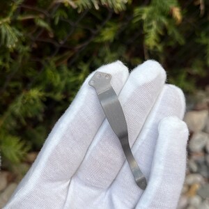 Op de afbeelding: Een zilveren metalen zakclip met een gebogen ontwerp en een puntige punt.