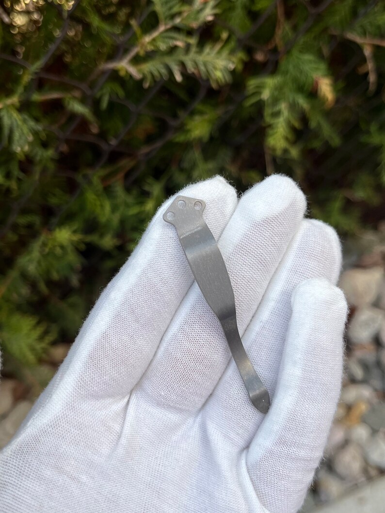 Op de afbeelding: Een zilveren metalen zakclip met een gebogen ontwerp en een puntige punt.