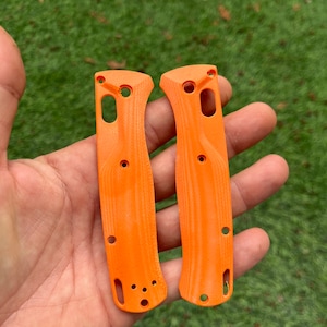 Puede incluir: Dos escamas de cuchillo de plástico naranja con una superficie texturizada y varios agujeros.