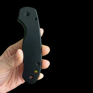 May include: Black knife handle with four screw holes. The handle is made of a smooth, matt material.