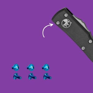 Puede incluir: Cinco tornillos azules con una navaja de bolsillo negra en el fondo. La navaja tiene un logotipo plateado de una pata de lobo.