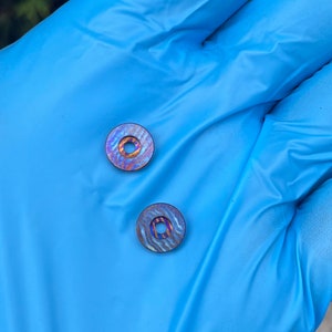 May include: Two small, iridescent, circular objects with a central hole. The objects display a swirling pattern of blues, purples, and golds. The items are set against a blue background.