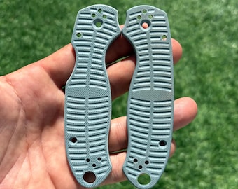 May include: Two light blue knife handle scales featuring a textured, ribbed surface pattern. Each piece has a curved shape with multiple pre-drilled circular holes for assembly, designed to fit securely on both sides of a folding knife frame.