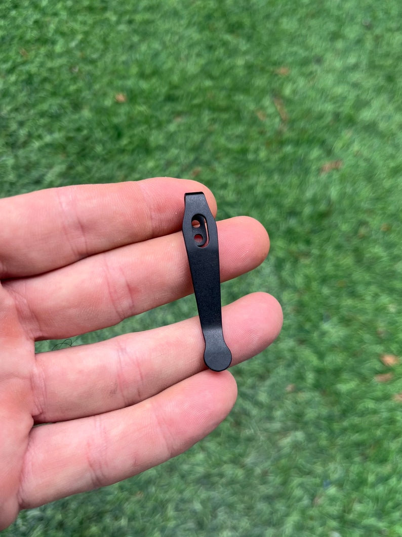 May include: Black metal pocket clip with a rounded end and a single hole.