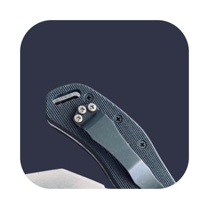 K&ouml;nnte beinhalten: Ein schwarzes Taschenmesser mit einem strukturierten Griff und einem schwarzen Taschenclip. Das Messer hat eine silberne Klinge und ein kleines Loch f&uuml;r eine Schnur.