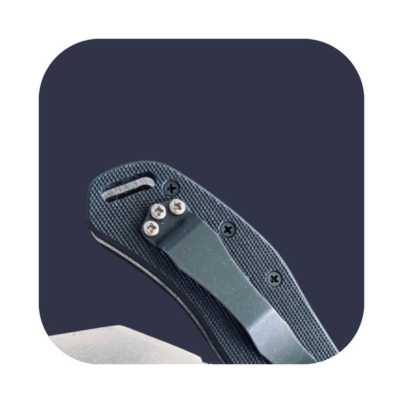 K&ouml;nnte beinhalten: Ein schwarzes Taschenmesser mit einem strukturierten Griff und einem schwarzen Taschenclip. Das Messer hat eine silberne Klinge und ein kleines Loch f&uuml;r eine Schnur.