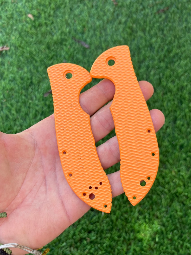 May include: Two orange knife scales with a textured surface and multiple holes. The scales are designed to fit a pocket knife.