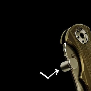May include: A close-up of a folding knife with a bronze-coloured, textured handle and a silver cylindrical thumb stud. The knife is set against a black background, with a white arrow pointing to the thumb stud.