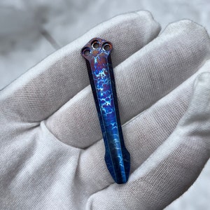 May include: A blue and copper titanium pen with a unique swirling pattern and three holes at the top.