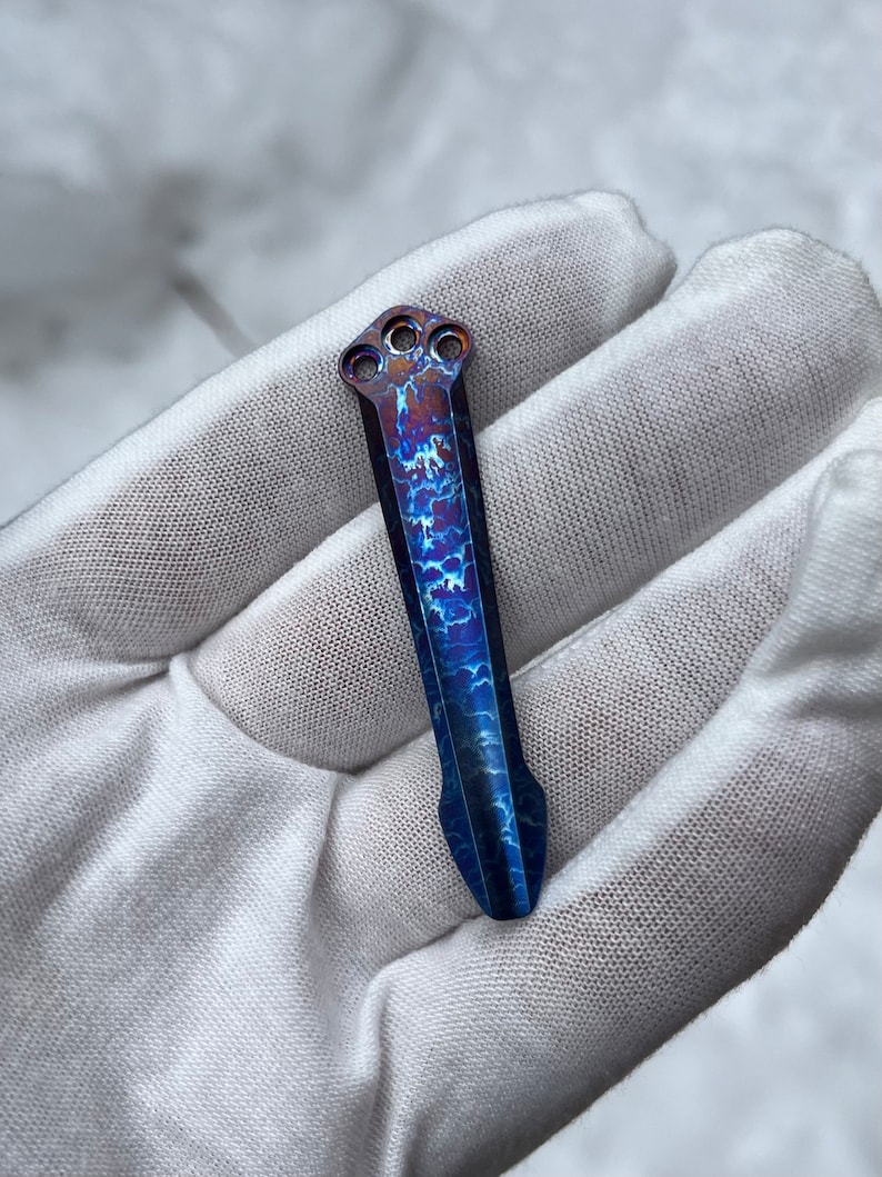 May include: A blue and copper titanium pen with a unique swirling pattern and three holes at the top.