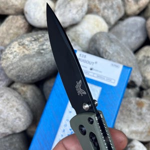 May include: A black and green pocket knife with a partially open blade. The blade has a black finish and the handle is green with a textured pattern. The knife has a butterfly logo on the blade and the text "535 BUGOUT" on the box.