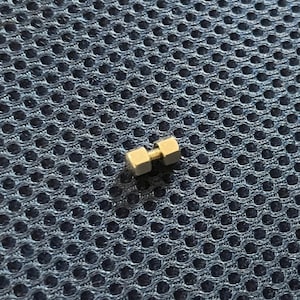 May include: A close-up of a small, gold-colored metal connector with a threaded center. The connector is made of two hexagonal pieces joined together.