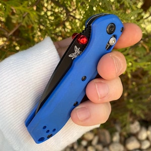 May include: A blue pocket knife with a black blade and a red button. The knife has a butterfly logo on the handle.