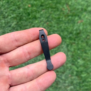 May include: Black metal key chain with two holes and a rounded end.
