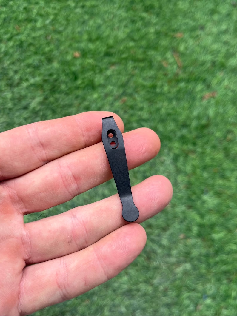 May include: Black metal key chain with two holes and a rounded end.