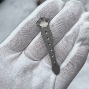 May include: A silver titanium pocket knife handle with a textured surface and a rounded tip.