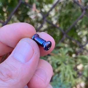 May include: A close-up of a small, iridescent blue and purple metal screw with a hexagonal head.