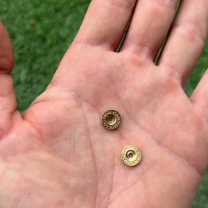 May include: Two gold-coloured metal rounds with the text "COLT AUTOMATIC PISTOL" engraved on them.