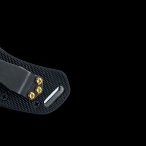 Puede incluir: Primer plano de una navaja de bolsillo negra con mango texturizado y clip. La navaja tiene tornillos de color dorado.