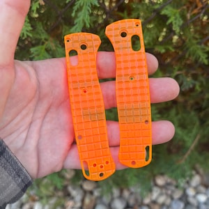Puede incluir: Dos escamas de cuchillo de plástico naranja brillante con una superficie texturizada. Las escamas están diseñadas para adaptarse a un cuchillo de bolsillo.