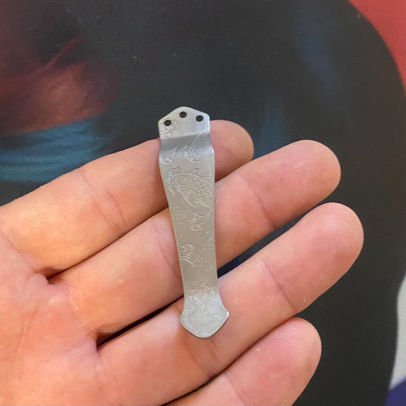 Pu&ograve; includere: Un fermaglio da tasca in argento con un design inciso decorativo. Il fermaglio ha tre fori nella parte superiore e una punta appuntita.