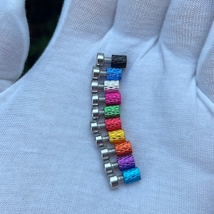 Puede incluir: Una fila de tornillos de metal de colores con cabezas plateadas. Los tornillos están dispuestos en un patrón de arcoíris, comenzando con negro y terminando con azul.