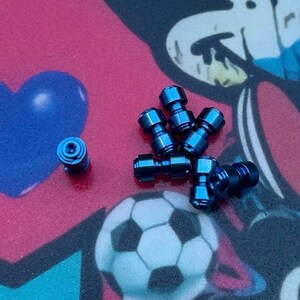 May include: A collection of small, metallic blue objects, possibly fasteners or hardware components, are scattered across a colorful background. The background features a heart shape, a soccer ball, and abstract designs in blue, red, and black.