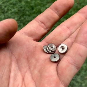 以下が含まれることがあります： 中央に小さな穴があり、縁が盛り上がった、銀色の丸い金属製のノブが5つあります。
