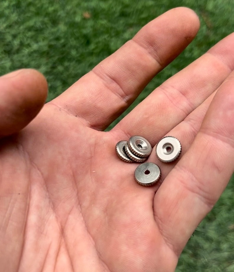 以下が含まれることがあります： 中央に小さな穴があり、縁が盛り上がった、銀色の丸い金属製のノブが5つあります。